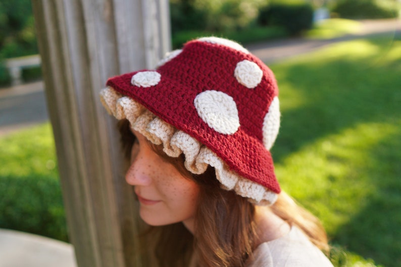 May include: A red crocheted hat shaped like a mushroom with white polka dots and a white crocheted ruffle around the brim.
