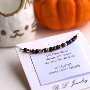 Puede incluir: Un collar de granate chapado en oro de 14 quilates con un mensaje en código Morse. La tarjeta dice "14k Gold Plated Nature Birthstone Morse Code Necklace Jan-Garnet Morse code - Patricia R. L. Jewelry".