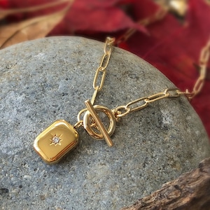 Peut inclure: Un collier en chaîne dorée avec un pendentif rectangulaire orné d'une petite pierre transparente. Le collier a un fermoir à bascule.