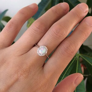 May include: A silver ring with a white opal gemstone surrounded by a halo of smaller clear gemstones.