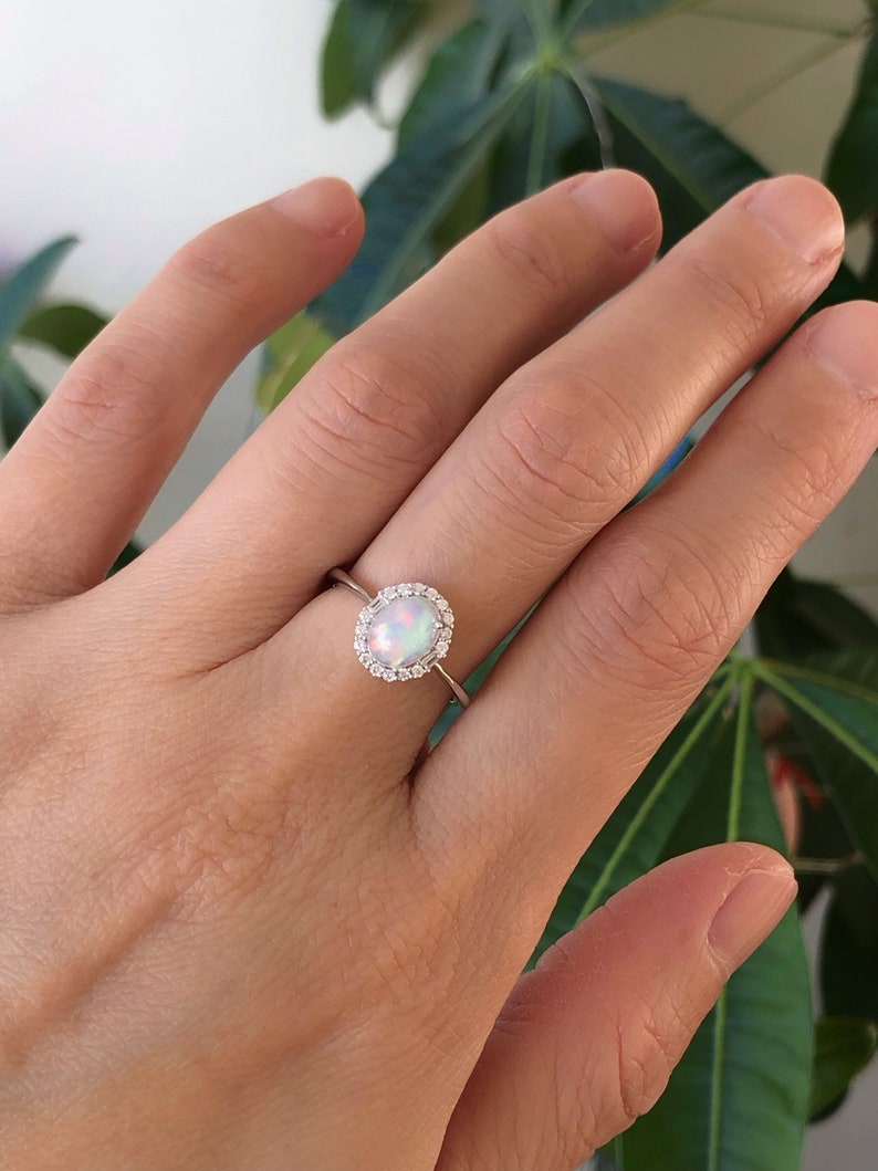 May include: A silver ring with a white opal gemstone surrounded by a halo of smaller clear gemstones.