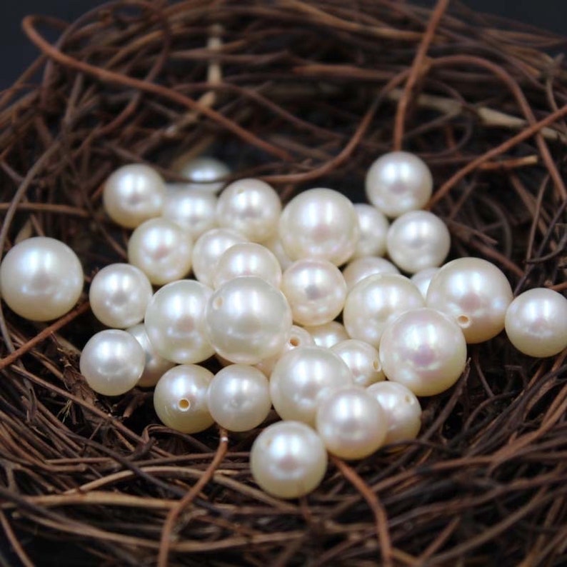 May include: A collection of white pearl beads in a brown nest-like container. The pearls are round and smooth, with a slight iridescent sheen.