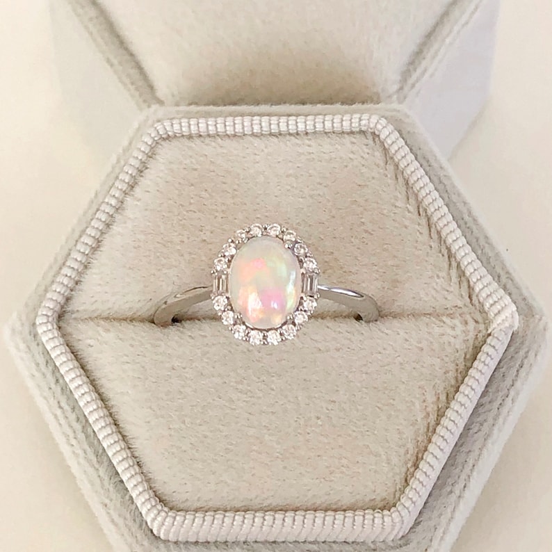 May include: A silver ring with a white opal gemstone surrounded by a halo of small diamonds.