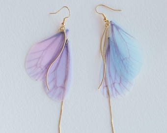 May include: A pair of dangle earrings with delicate butterfly wings made of iridescent blue and purple fabric. The wings are attached to a gold chain that hangs down from the earring.