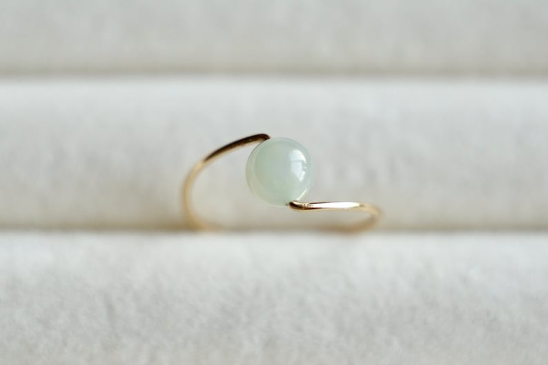 May include: A delicate gold ring with a single, round, light green gemstone set in the center.