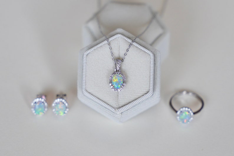 May include: A set of opal jewelry including a necklace, earrings, and a ring. The jewelry is silver with a white opal stone in each piece. The necklace is in a white box.