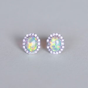 May include: A pair of silver earrings with oval-shaped opal gemstones surrounded by a halo of small clear stones.