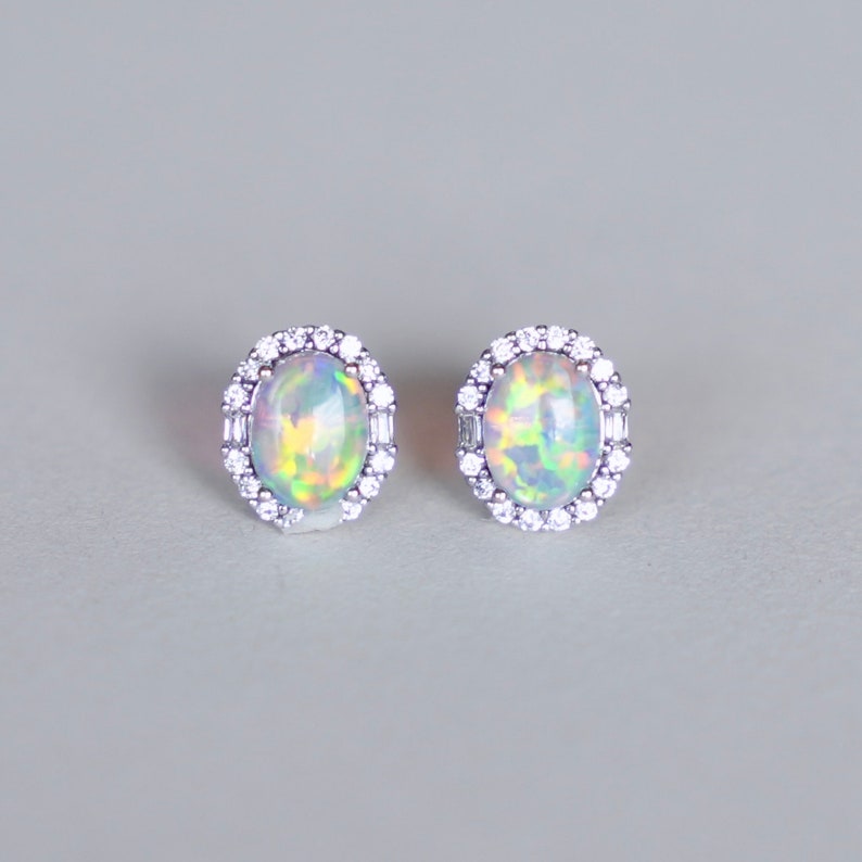 May include: A pair of silver earrings with oval-shaped opal gemstones surrounded by a halo of small clear stones.