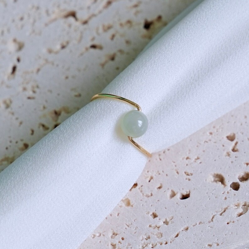 May include: A gold ring with a light green gemstone. The ring is simple and elegant.