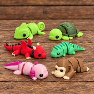 May include: A collection of six articulated animal figurines including a green chameleon, a green turtle, a red dragon, a green lizard, a pink axolotl, and a brown monkey. Each figure features a segmented body design with black eyes.
