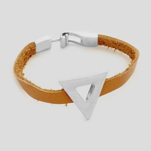 Puede incluir: Una pulsera de cuero marrón claro con un triángulo plateado. La pulsera tiene un diseño sencillo con un cierre de hebilla. El triángulo es una forma geométrica sólida con un centro recortado.