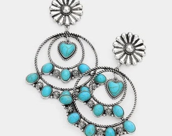 Puede incluir: Pendientes plateados con piedras de color turquesa y una parte superior en forma de margarita. Los pendientes presentan una piedra turquesa en forma de corazón y múltiples piedras turquesas ovaladas. El diseño incluye elementos circulares en capas.