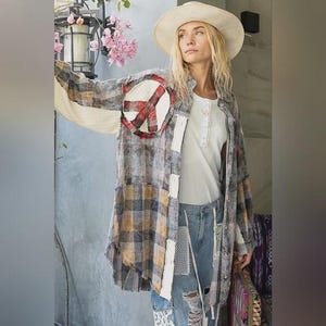 Może przedstawiać: Koszula w kratę z naszywką w kształcie znaku pokoju. Koszula ma mieszankę szarych, brązowych i żółtych wzorów w kratę, z białymi naszywkami i postarzanymi detalami. Osoba ma na sobie biały top i niebieskie dżinsy z kapeluszem z szerokim rondem.