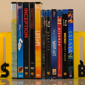 Puede incluir: Una colecci&oacute;n de DVDs y Blu-ray se mantiene entre sujetalibros amarillos con la palabra "PITTSBURGH" en letras negras. Los t&iacute;tulos de las pel&iacute;culas incluyen "Up", "Inception" y "Mad Max: Fury Road".