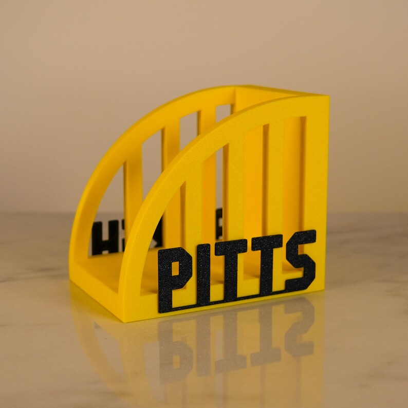 Puede incluir: Un organizador de escritorio amarillo con la palabra "PITTS" en letras negras. El organizador tiene un dise&ntilde;o arqueado con divisores verticales. Las letras "H" y "S" tambi&eacute;n son visibles en el lateral.