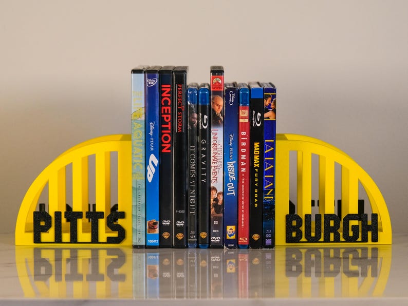 Puede incluir: Un juego de sujetalibros amarillos con la palabra "Pittsburgh" en negro. Soportan una colecci&oacute;n de DVD y Blu-ray, incluyendo "Up", "Inception" y "La La Land".