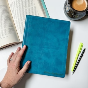 May include: A teal blue leather-bound journal with the name "Karen Liz Stevenson" written in cursive on the front cover.