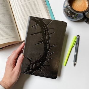 May include: A black leather-bound journal with a crown of thorns design embossed on the cover. The journal is titled "Vanderbloemen"