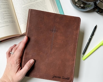 Puede incluir: Una funda de Biblia de piel sintética marrón con un diseño de cruz en relieve en el centro y el nombre Jaine Scott grabado en la esquina inferior derecha. La funda tiene costuras visibles en los bordes y un acabado de superficie texturizado.