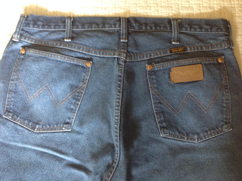 Puede incluir: Primer plano de la parte trasera de unos vaqueros azules. Los vaqueros tienen dos bolsillos traseros con una costura en forma de 'W' en hilo naranja. Una etiqueta de cuero marr&oacute;n con el nombre de la marca es visible en el bolsillo derecho. Remaches de cobre.
