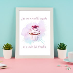May include: A white framed print with a watercolour illustration of a cupcake with pink frosting and raspberries on top. The text "You are a beautiful cupcake in a world full of muffins" is printed below the cupcake.