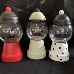 May include: Three glass candy jars with black lids and different colored bases. The jars are decorated with polka dots. The bases are red, green, and white.
