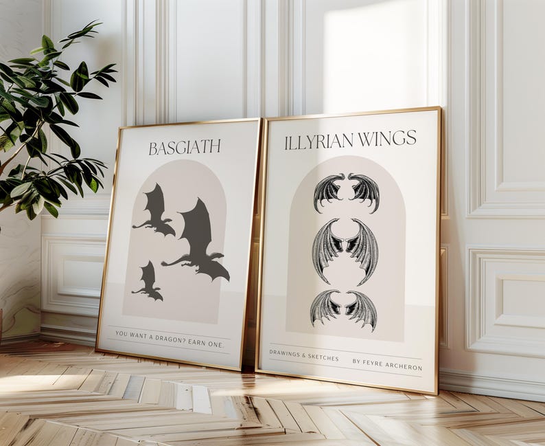 May include: Two gold-framed prints featuring dragon illustrations.  The left print, titled 'Basgiath,' shows three black silhouettes of dragons against a beige archway on a blush-pink background. The right print, ' Illyrian Wings,' displays three pairs of black wings in a similar archway design. Both prints include text detailing the artwork and artist, Feyre Archeron.