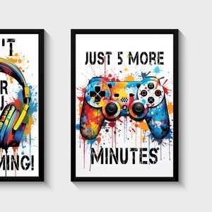 Puede incluir: Dos impresiones enmarcadas con un tema de juego. La primera impresi&oacute;n presenta unos auriculares con salpicaduras de pintura de colores. La segunda impresi&oacute;n presenta un mando de videojuego de colores con el texto "JUST 5 MORE MINUTES".