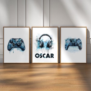 May include: Three framed prints with watercolor illustrations of gaming accessories. The left print features a blue and black video game controller. The middle print features blue headphones with the name "OSCAR" in black text. The right print features a blue and black video game controller.