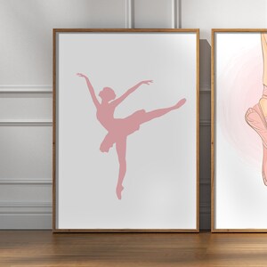 May include: Two framed art prints. The left print features a pink silhouette of a ballerina in a graceful pose. The right print shows a close-up of pink ballet pointe shoes. Both prints have a white background and are in wooden frames.