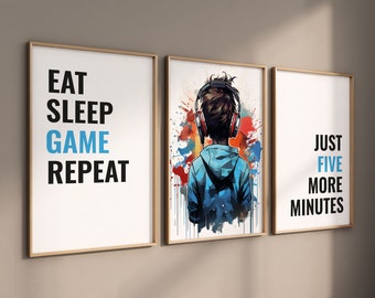 May include: Three framed art prints with a gaming theme. The left print reads "EAT SLEEP GAME REPEAT" in black and blue text. The center print features a person wearing headphones, with colorful paint splatters. The right print says "JUST FIVE MORE MINUTES".