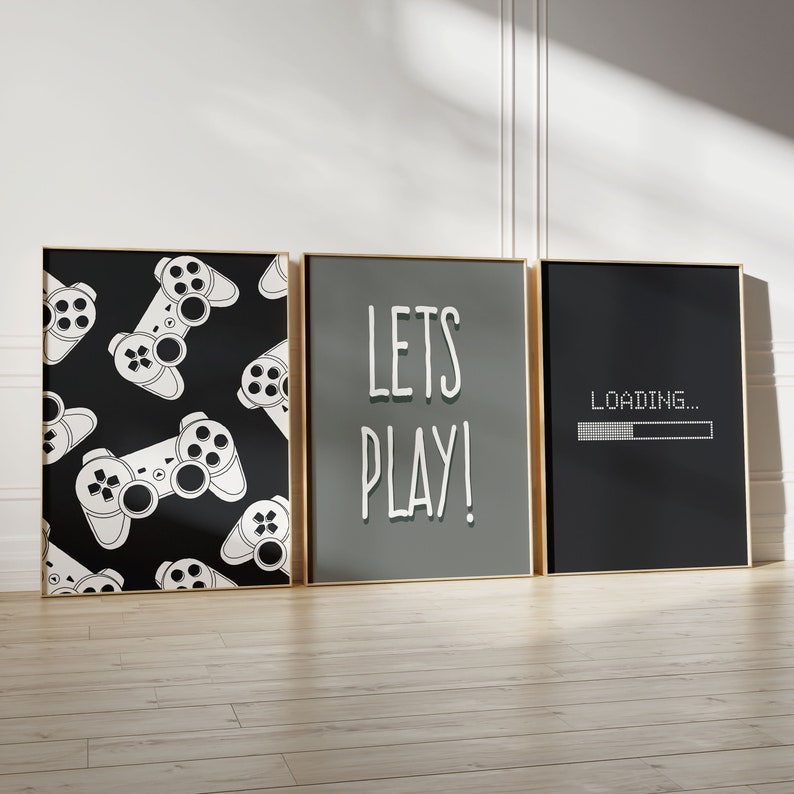 Puede incluir: Tres impresiones enmarcadas con tem&aacute;tica de juegos. La impresi&oacute;n de la izquierda presenta un patr&oacute;n en blanco y negro de mandos de videojuegos. La impresi&oacute;n del medio tiene el texto "LETS PLAY!" en blanco sobre un fondo gris. La impresi&oacute;n de la derecha tiene el texto "LOADING..." en blanco sobre un fondo negro con una barra de progreso.