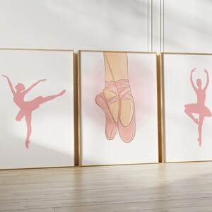 May include: Three framed art prints featuring ballet-themed illustrations. The prints showcase pink silhouettes of ballerinas in various poses and a close-up of ballet shoes. The frames have a gold finish, and the background is white.