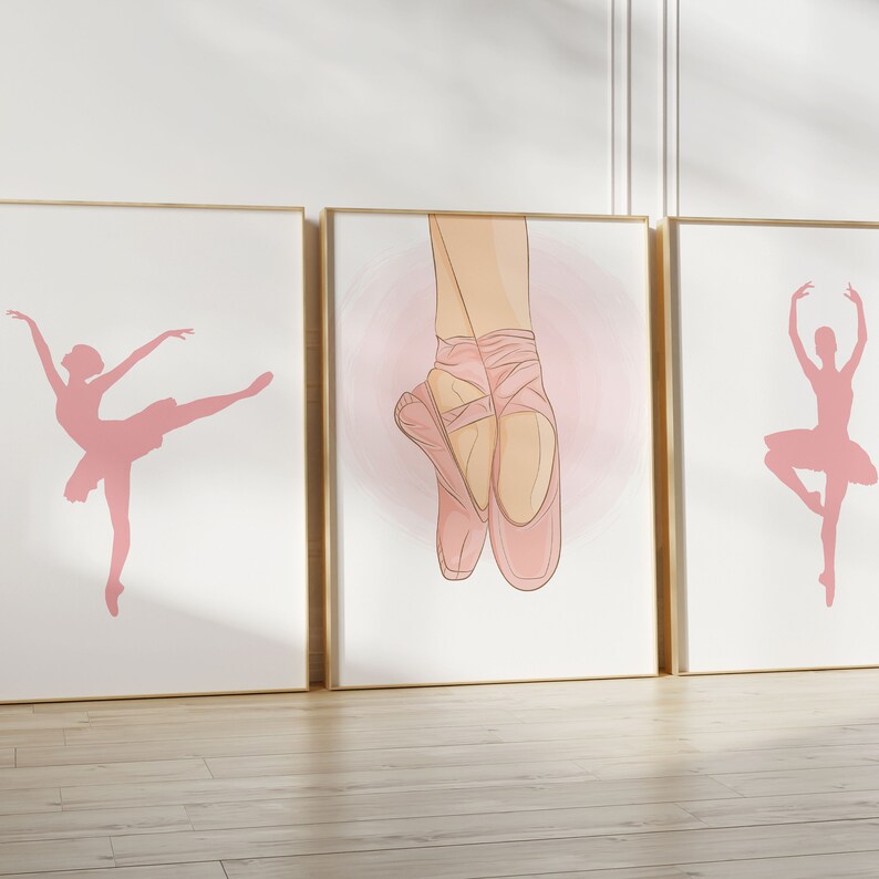 May include: Three framed art prints featuring ballet-themed illustrations. The prints showcase pink silhouettes of ballerinas in various poses and a close-up of ballet shoes. The frames have a gold finish, and the background is white.