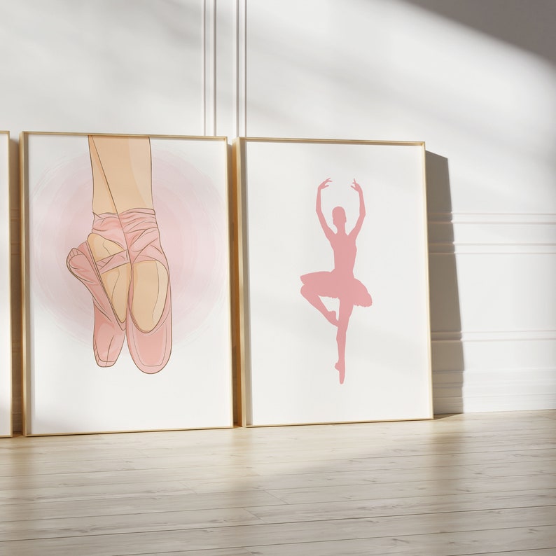 May include: Three framed art prints featuring ballet themes. One print shows a pair of ballet shoes, another a ballerina silhouette, and the third is partially visible. The prints have a white background with pink accents and gold frames.