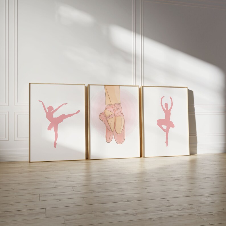 May include: Three framed art prints featuring ballet-themed illustrations. The prints showcase pink silhouettes of a ballerina in various poses and a close-up of ballet shoes. The frames have a gold finish, and the background is white.