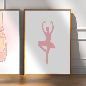 May include: Two framed art prints. One features a pair of pink ballet pointe shoes. The other print shows a pink silhouette of a ballerina in a graceful pose, wearing a tutu. Both prints have a white background and are in wooden frames.