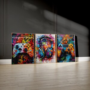 Pu&ograve; includere: Tre stampe su tela incorniciate con sfondi astratti colorati. La stampa a sinistra presenta un controller per videogiochi, la stampa al centro presenta un paio di cuffie e la stampa a destra presenta un controller per videogiochi.