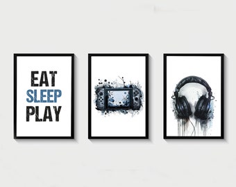 Könnte beinhalten: Drei schwarze gerahmte Drucke mit weißen Hintergründen. Der linke Druck hat den Text "EAT SLEEP PLAY" in Schwarz und Blau. Der mittlere Druck hat eine schwarze und blaue Aquarell-Illustration einer Videospielkonsole. Der rechte Druck hat eine schwarze und blaue Aquarell-Illustration von Kopfhörern.