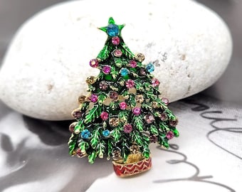 May include: A green Christmas tree brooch with a red and gold pot. The tree is decorated with colorful rhinestones.