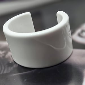May include: A white ceramic bangle bracelet with a smooth, glossy finish.