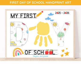 May include: A framed print with the text "MY FIRST DAY OF SCHOOL HANDPRINT ART." The artwork features a yellow handprint, colorful drawings, and the text "2-25-2-26." The bottom of the print reads "Taylor, 2nd grade."