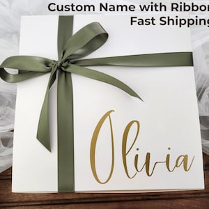 May include: A white gift box tied with a sage green ribbon. The name "Olivia" is written in gold script on the front. The text "Custom Name with Ribbon" is at the top.