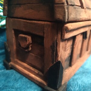 Puede incluir: Un cofre del tesoro de madera con un acabado marr&oacute;n oscuro y detalles en metal negro. El cofre tiene una tapa con bisagras y un cierre de metal decorativo.