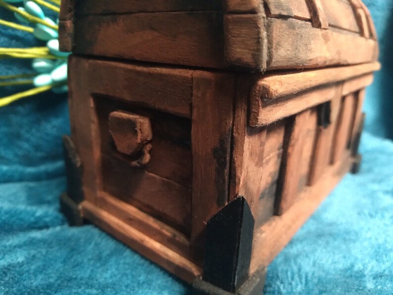 Puede incluir: Un cofre del tesoro de madera con un acabado marr&oacute;n oscuro y detalles en metal negro. El cofre tiene una tapa con bisagras y un cierre de metal decorativo.