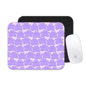 May include: A computer mouse and mousepad set. The mousepad features a repeating pattern of purple Ditto characters on a light pink background. A white Apple mouse is positioned to the right of the mousepad, with the Apple logo visible.