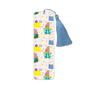 May include: A rectangular bookmark featuring a repeating pattern of cartoon bunnies in colorful outfits. The bookmark has a light blue tassel attached to the top. The background is a light beige with small floral designs.