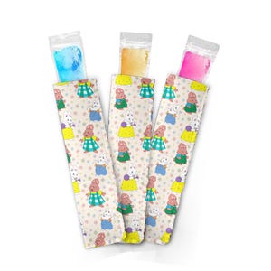 May include: Three colorful freezer pop sleeves with a repeating pattern of a cartoon bunny in various outfits. Each sleeve holds a different colored powder: blue, yellow, and pink. The sleeves are on a white background.
