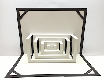 May include: A white pop-up card with a black frame and a series of nested squares that create an optical illusion.