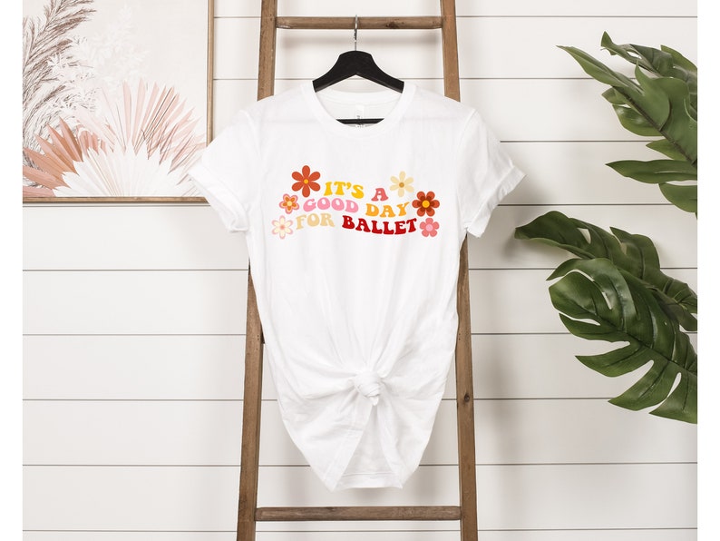 May include: White t-shirt with a graphic print of colorful flowers and the text "It's a good day for ballet".
